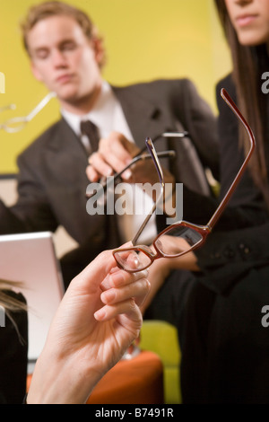 Hände halten Brillen mit Geschäftsleuten im Hintergrund Stockfoto
