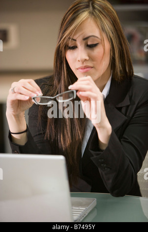 Junge weibliche Büroangestellte sitzen am Schreibtisch mit Laptop, die Brille zu betrachten Stockfoto