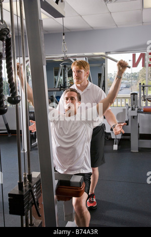 Mann mittleren Alters Heben von Gewichten im Fitnessstudio mit personal trainer Stockfoto