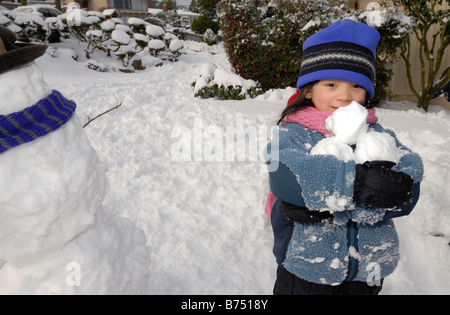 4 Jahre altes Mädchen hält drei Schneebälle. Stockfoto
