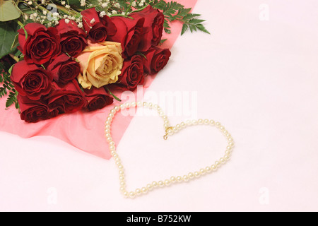 Stillleben mit roter Rosen mit einer gelben Rose im Zentrum und eine Perlenkette in der Form eines Herzens auf weißem Hintergrund Stockfoto