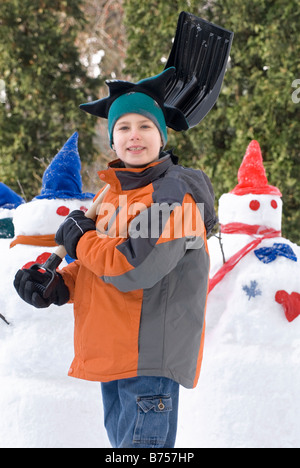 Zehn Jahre alter Junge mit Schaufel neben Schneemänner, Winnipeg, Kanada Stockfoto