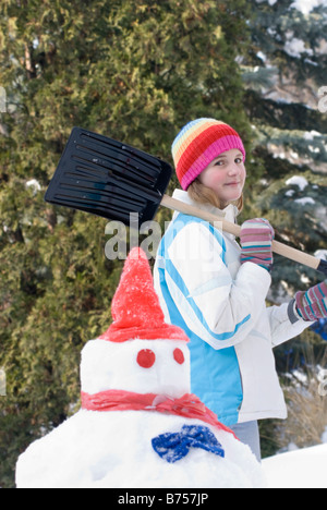 Dreizehn Jahre altes Mädchen mit Schaufel neben Schneemänner, Winnipeg, Kanada Stockfoto