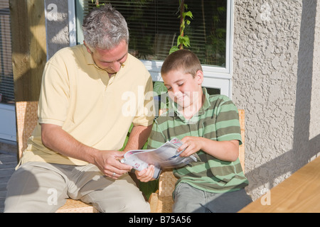 Vater und Sohn betrachten Magazin, sitzen auf dem Deck, Winnipeg, Kanada Stockfoto