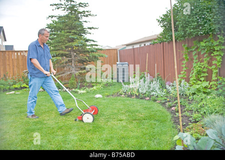 Ältere Mann mit Reel Rasenmäher im Hinterhof, Winnipeg, Manitoba, Kanada Stockfoto