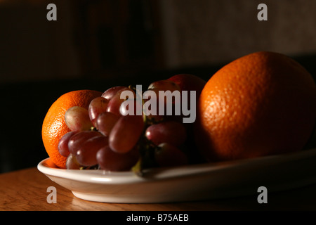 ein Stillleben Foto von etwas Obst in einer Obstschale einschließlich Orangen Äpfel und rote Trauben Stockfoto