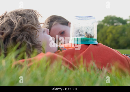 Sechs Jahre alten Jungen und 8 Jahre alten Mädchen, Verlegung auf Rasen mit Frosch im Sammeln von Glas, Winnipeg, Kanada Stockfoto