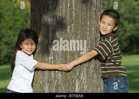 Fünf Jahre alte Schwester und sieben Jahre alten Bruder halten Hände um Baum, Winnipeg, Manitoba, Kanada Stockfoto