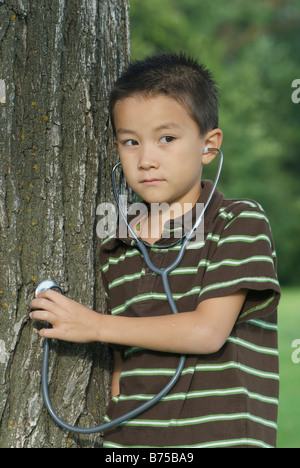 Sieben Jahre alter Junge mit Stethescope platziert auf Baum, Winnipeg, Kanada Stockfoto