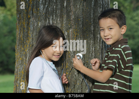 Fünf Jahre alte Schwester und sieben Jahre alten Bruder mit Stethoskop auf Baum, Winnipeg, Manitoba, Kanada Stockfoto