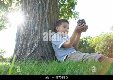 Sechs Jahre alte junge hält Kleinbaum, setzte neben Großbaum, Winnipeg, Kanada Stockfoto