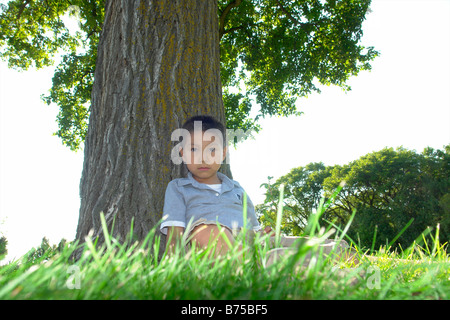 Sechs Jahre alter Junge sitzt neben Großbaum, Winnipeg, Manitoba, Kanada Stockfoto