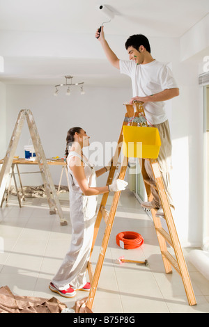 Junger Mann Malerei der Wand und eine junge Frau hält eine Trittleiter Stockfoto