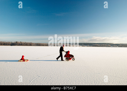 Mutter mit Kinderwagen ziehen ein Kind im Schlitten auf zugefrorenen See, Lohja, Finnland Stockfoto