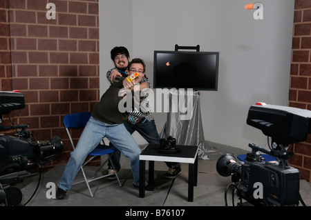 Akteure auf der Bühne ein TV-Studio set mit Host versucht, Berserker Gast Spielzeug Pistole schießen zu kontrollieren Stockfoto