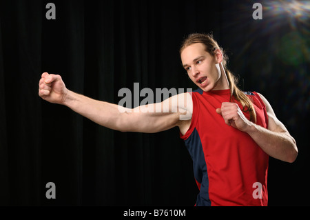 Junger Mann mit langen Haaren üben einen schwenkbaren Karate Schlag während schreien im Rampenlicht Stockfoto