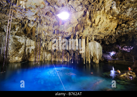 VALLADOLID, Mexiko – einheimische und besuchende Schwimmer genießen das kristallklare Wasser von Cenote X'kakah in der Nähe von Valladolid, Yucatan. Das natürliche Kalkstein-Schwimmloch verfügt über dramatische Stalaktiten, die von der Decke hängen und durch eine kleine Öffnung darüber natürliches Licht erhalten. Dieser unterirdische Pool ist Teil des riesigen Netzes unterirdischer Wasserstraßen unter der Halbinsel Yucatan. Stockfoto