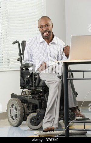 Porträt eines Geschäftsmannes mit zerebraler Lähmung in einem Rollstuhl sitzen und arbeiten auf einem Computer mit seinem Fuß Stockfoto