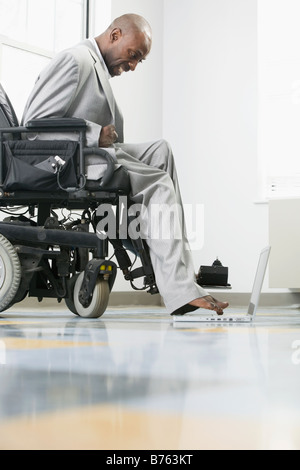 Geschäftsmann mit zerebraler Lähmung im Rollstuhl arbeiten auf einem Laptop mit seinem Fuß Stockfoto