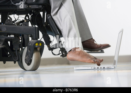 Niedrige Schnittansicht eines Geschäftsmannes mit zerebraler Lähmung in einem Rollstuhl sitzen und arbeiten auf einem Laptop mit seinem Fuß Stockfoto