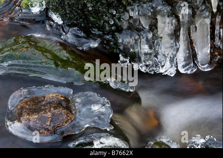 Eis bildete, auf Felsen in einem Bergbach mit Wasser rauschenden Vergangenheit Stockfoto