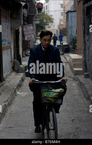 Mann Reiten Fahrrad allein an den ersten kalten Morgen im Jahr morgens eine Seitenstraße Gasse in Guangzhou China Black und Stockfoto