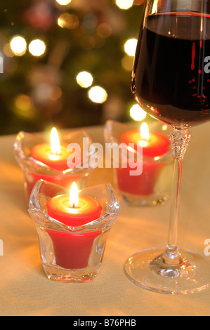 Weihnachten Urlaub Konzept mit Weinglas mit Rotwein gefüllt und beleuchtet rote votive-Kerzen am Tisch vor beleuchteten Baum Stockfoto