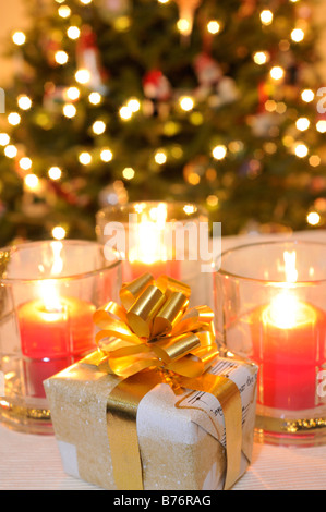 Wickelte Weihnachtsgeschenk mit Kerzen und beleuchteten Baum im Hintergrund Stockfoto