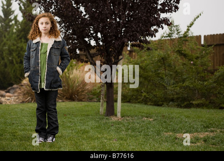 Ein wachsendes junges Mädchen steht vor einem jungen Bäumchen. Stockfoto