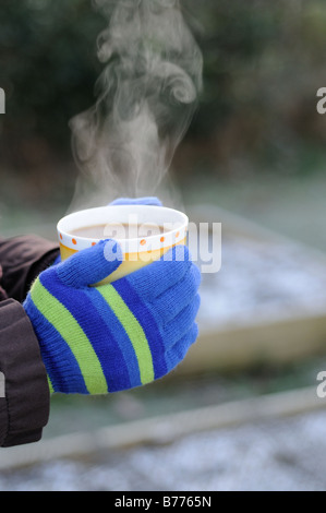 Lady Gärtner Hände in Handschuhe halten dampfenden Tasse Kaffee im Garten Januar Stockfoto