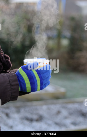 Lady Gärtner Hände in Handschuhe halten dampfenden Tasse Kaffee im Garten Januar Stockfoto