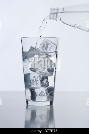 Wasser aus der Flasche ins Glas Eiswürfel gießen Stockfoto
