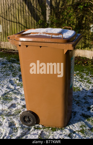 Ein großer brauner Garten Abfall Wheelie Bin mit Schnee am Deckel in einen Garten Cheshire England Großbritannien Stockfoto