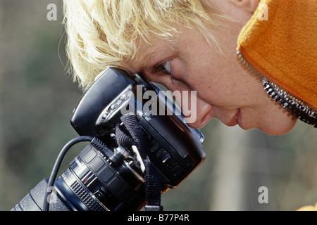 Blonde Frau, die durch eine Spiegelreflexkamera Stockfoto