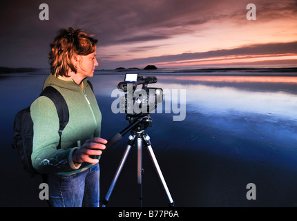 Kamerafrau bei Filmkamera filmt Sonnenuntergang mit einem Stativ an Meyers Creek Strand, Küste von Pistol River State Park, Oregon, Oregon Stockfoto