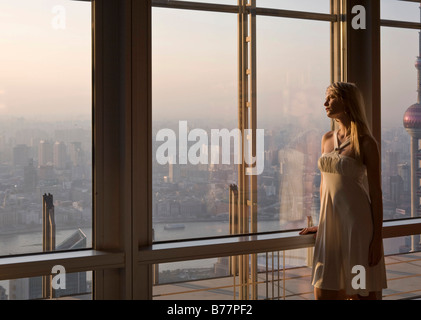 Junge Frau, Blick auf die Skyline durch ihre Fenster, Shanghai, China, Asien Stockfoto