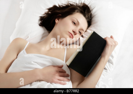 Junge Brünette Frau, die ein Buch im Bett lesen Stockfoto