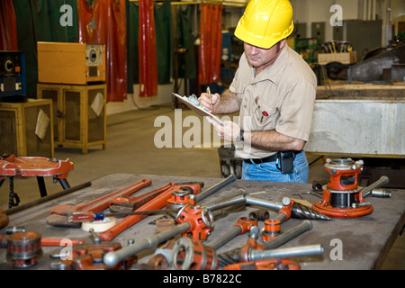 Prüfer der Inventur der Werkzeuge in einem Industriebetrieb Schweißen Ausrüstung ist im Hintergrund sichtbar Stockfoto