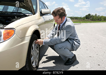 Ein Geschäftsmann hat einen Platten Reifen auf der Straße, er ist immer bereit, es zu ändern Stockfoto
