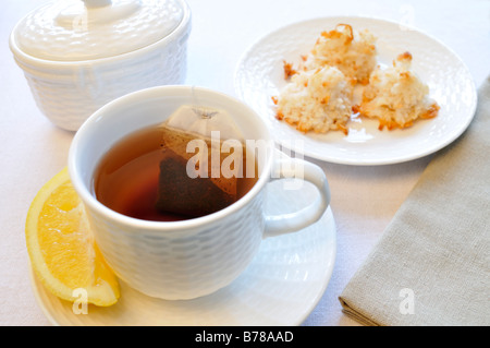 Eine Tasse schwarzen Tee mit einem Stück Zitrone, Zuckerdose und Teller mit Kokos Makronen Plätzchen mit einer Serviette auf weißem Hintergrund. Stockfoto