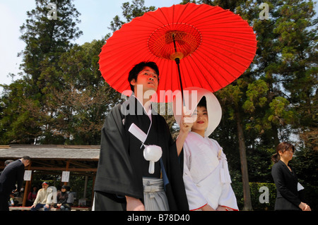 Japanische Hochzeitspaar tragen traditionelle Hochzeits-Kimonos, Braut trägt eine Haube, Bräutigam mit einem roten Sonnenschirm vor th Stockfoto