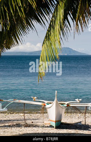 Philippinische Boot (Bangka) am steinigen Strand mit Palme im Vordergrund, Malabrigo, Batangas, Philippinen Stockfoto