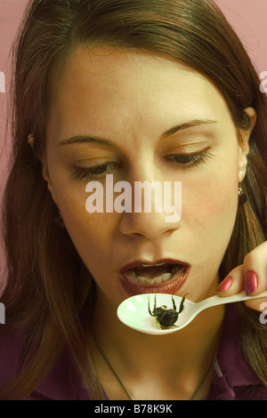 Junge Frau, eine tote Wanze aus einem Plastiklöffel zu essen vorbereiten.  -MODELL VERÖFFENTLICHT. Stockfoto