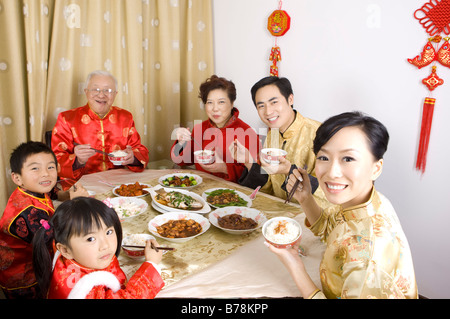 Familienmitglieder in traditioneller Kleidung mit Abendessen zusammen und lächelt in die Kamera Stockfoto