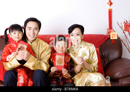 Junge Familie mit zwei Kindern in traditioneller Kleidung halten rote Umschläge und lächelt in die Kamera Stockfoto