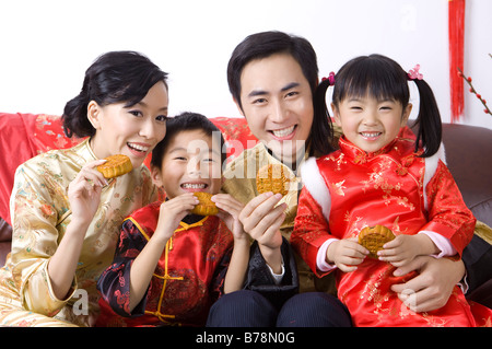 Junge Familie mit zwei Kindern in traditioneller Kleidung hält die Mondkuchen und lächelt in die Kamera Stockfoto