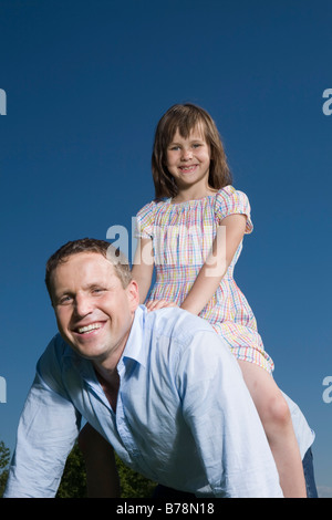 Kleines Mädchen ist (6-7) sitzen auf Vater zurück, Lächeln Stockfoto