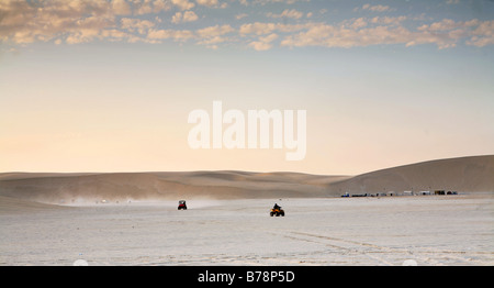 Quad-Biker spielen bei Sonnenuntergang auf den Salt Flats neben den Sanddünen in Mesaieed, Katar. Stockfoto