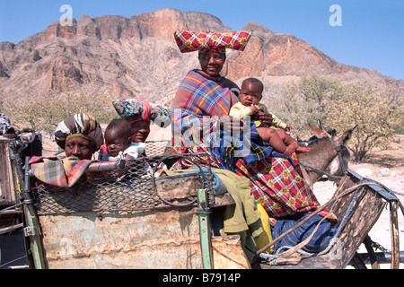 Herero Frauen in charakteristische Kleidung mit Babys auf einem Esel Warenkorb, Sesfontein, Kaokoveld, Namibia, Afrika Stockfoto