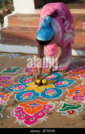 Indische Frau Inverkehrbringen Räucherstäbchen in ein Angebot von Blumen und Kuhmist auf einem Rangoli Design an Sankranti in einem indischen Straße. Andhra Pradesh, Indien Stockfoto
